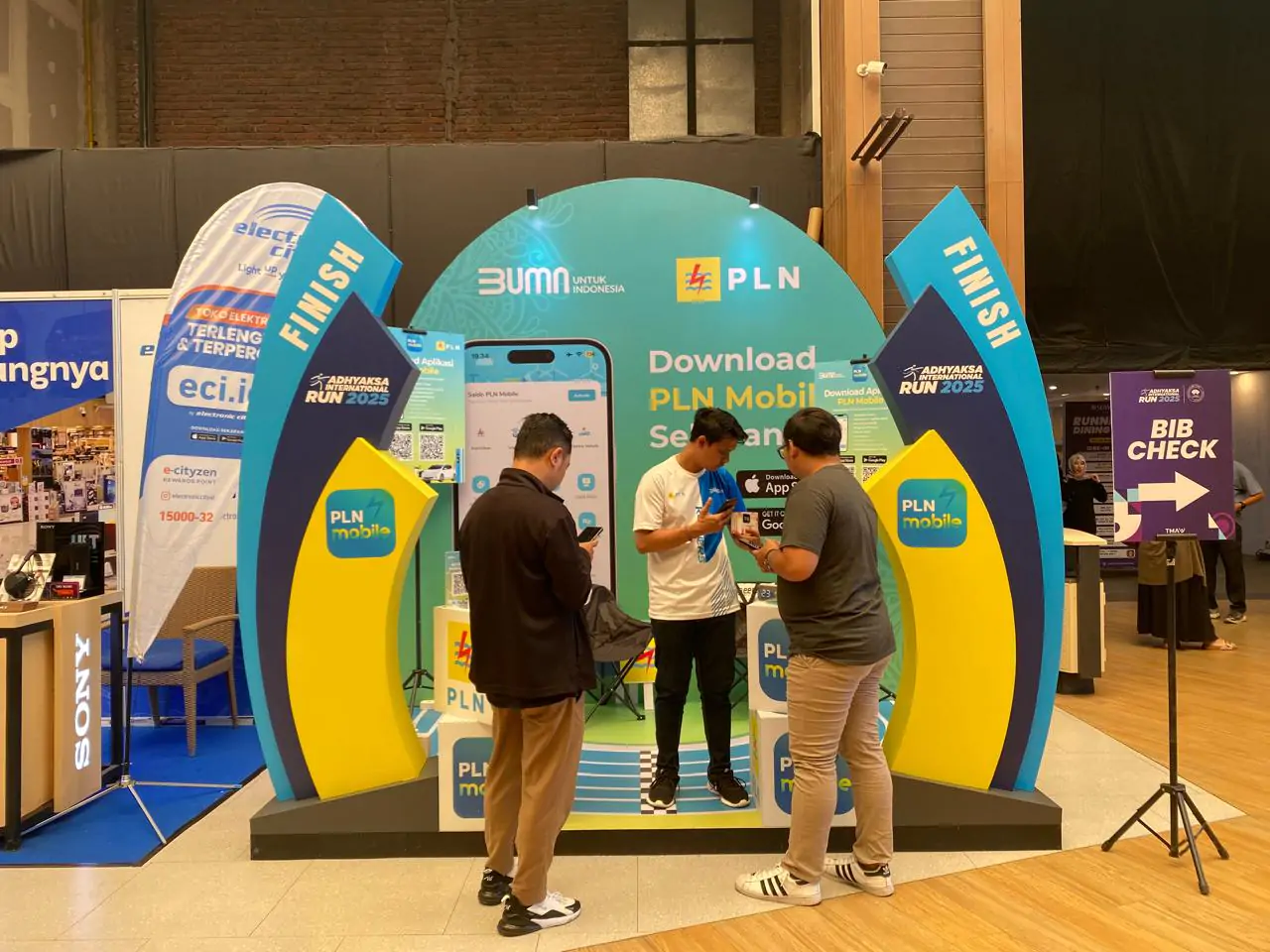 Beberapa pelari yang mendatangi booth PLN di penukaran race pack Adhyaksa International Run, mencoba langsung layanan PLN Mobile dengan panduan petugas.