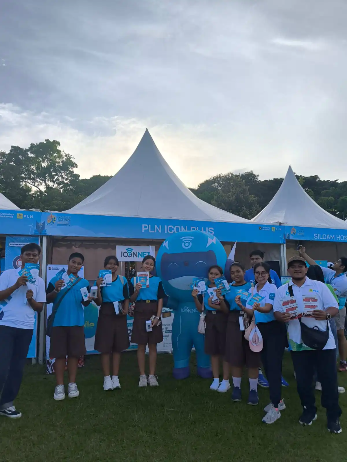 Petugas yang dikerahkan memanfaatkan kemeriahan PLN Bali Fun Run untuk mengoptimalkan promo power hero diskon 50%. Tampak petugas siap terjun membagikan brosur promo di depan booth.